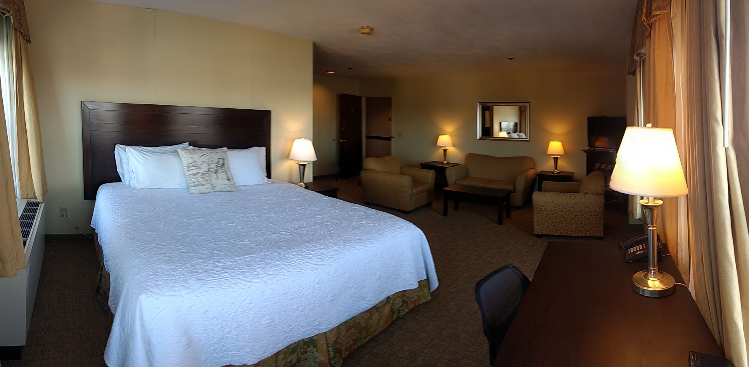 A hotel room with a large bed, two bedside tables with lamps, a chair, a desk, and a mirror on the wall.