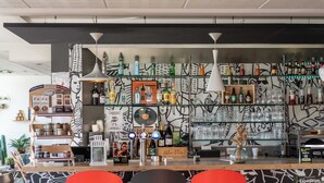 A bar area with shelves of bottles, a counter with taps, and a wall with a black and white abstract design. - B&B Hotel Limoges 3 (Limoges)