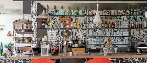 Una zona de bar con estanterías llenas de botellas, una barra con grifos y una pared decorada con un diseño abstracto en blanco y negro.
