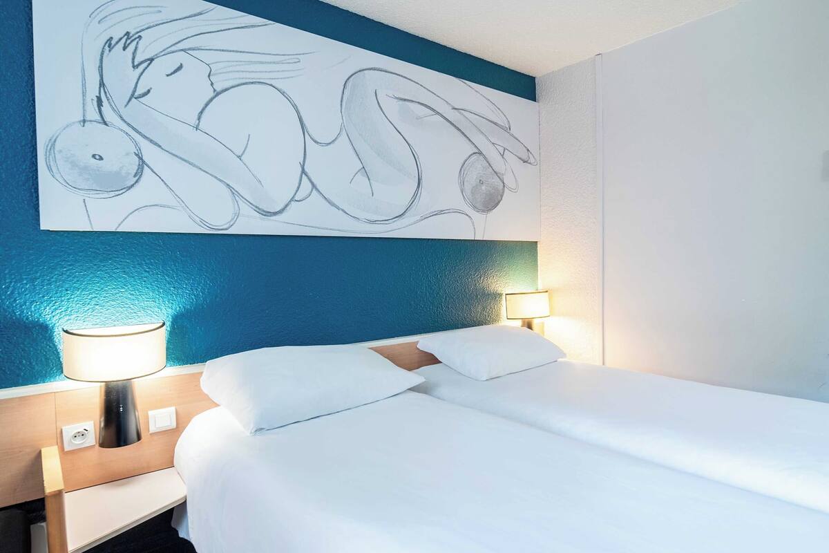 A hotel room with a bed, bedside lamps, a wall painting, and a blue accent wall.