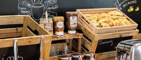 A café counter with wooden crates of croissants, jars of jam, and a toaster.