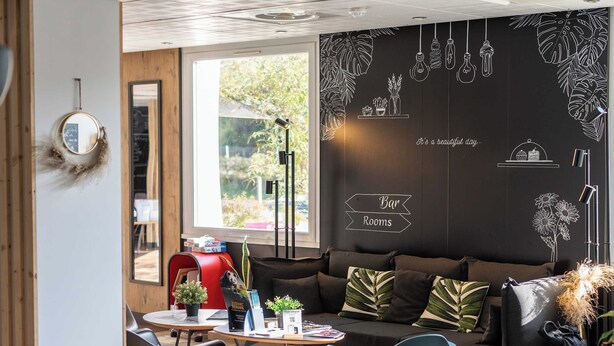 A modern interior with a sofa, chairs, a table, and a wall with decorative elements. - B&B Hotel Limoges 3 (Limoges)