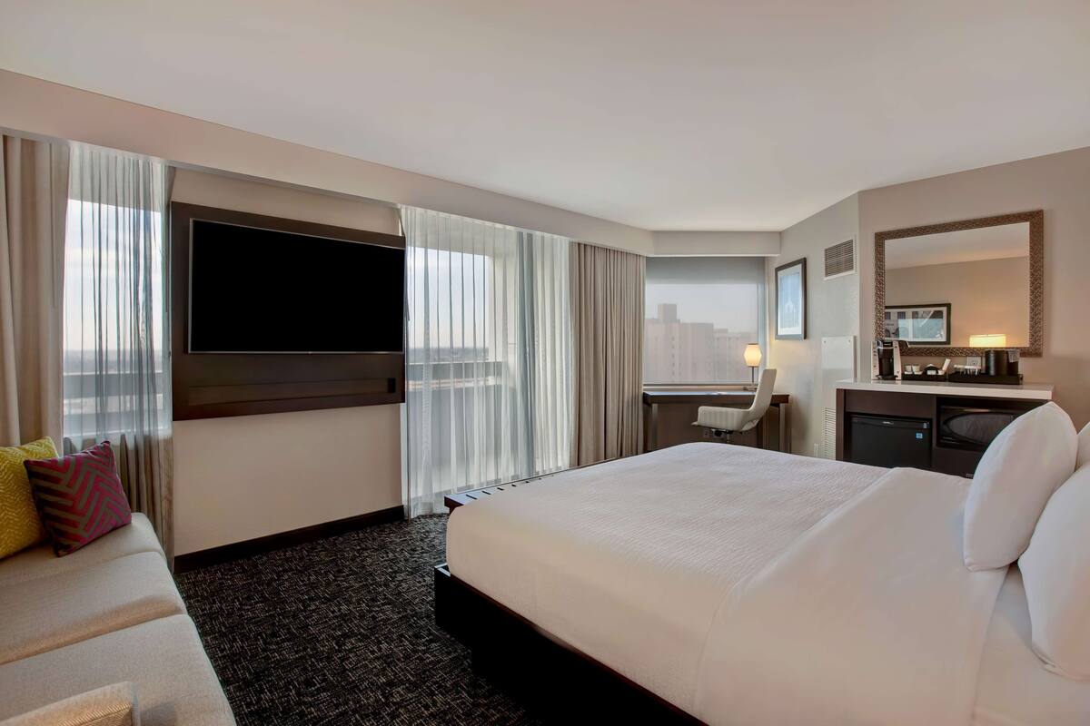 A hotel room with a large bed, a desk, a television, and a city view.