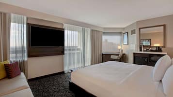 A hotel room with a large bed, a desk, a television, and a city view.