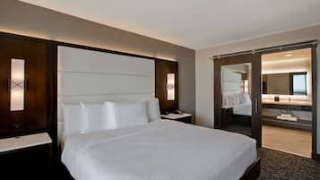 A hotel room with a large bed, a bedside table, a nightstand, a mirror, and a sliding door leading to a bathroom.