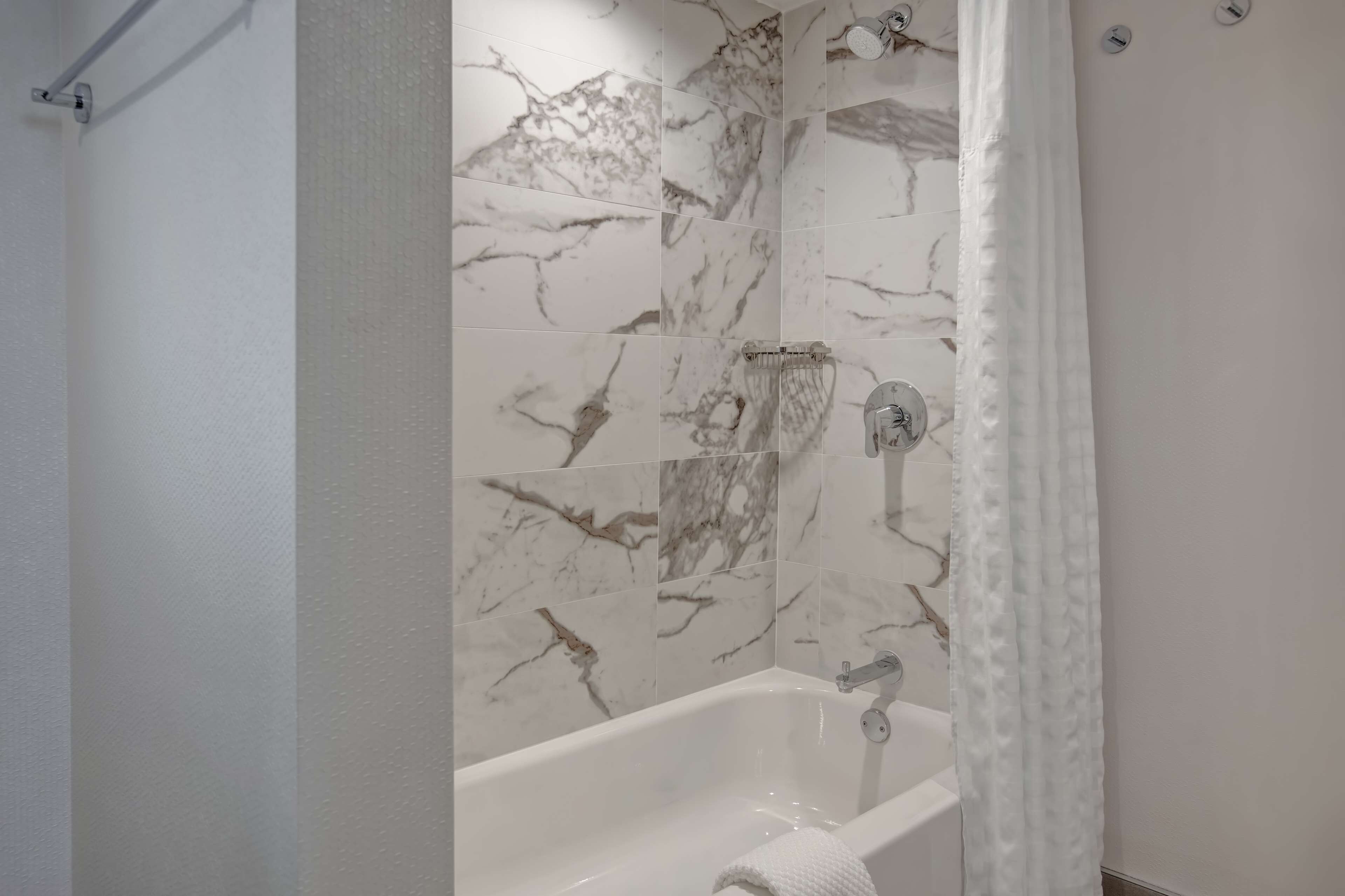 A bathroom with a white bathtub, marble-patterned walls, and a shower curtain.