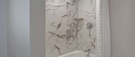 A bathroom with a white bathtub, marble-patterned walls, and a shower curtain.