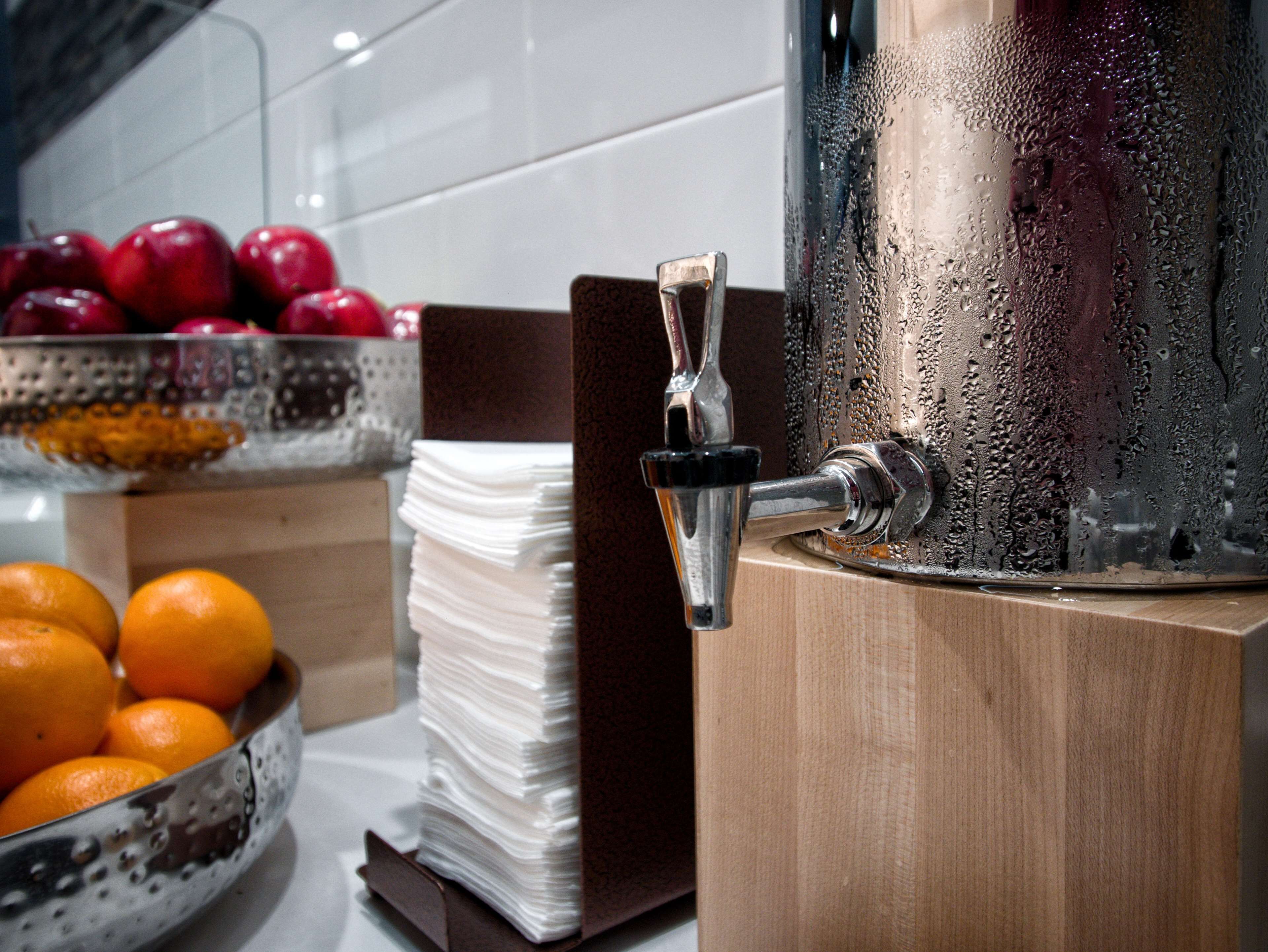 A beverage dispenser with a spout, a bowl of oranges, and a stack of napkins.