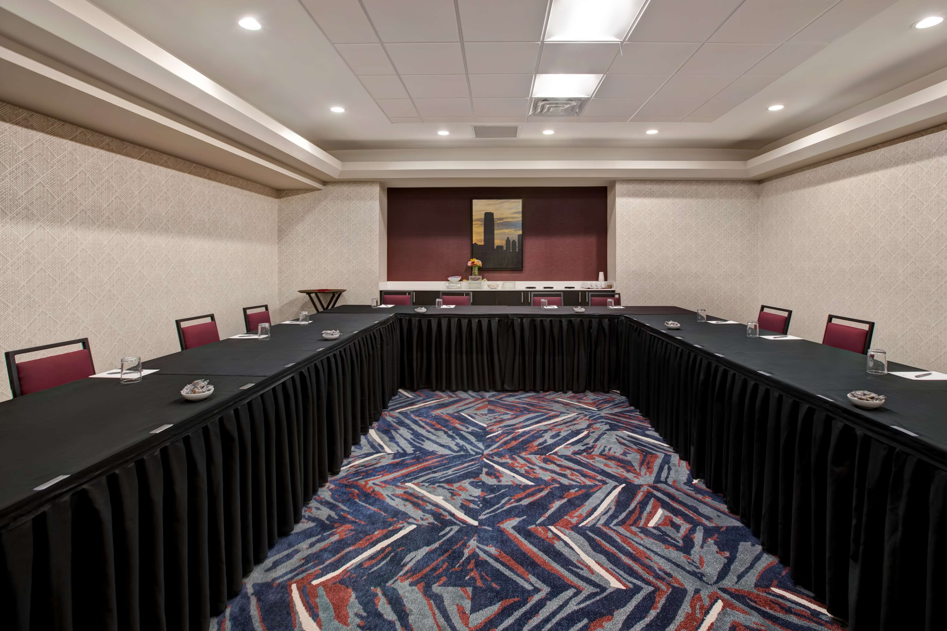 A conference room with a long table, red chairs, and a patterned carpet.