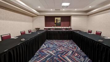 A conference room with a long table, red chairs, and a patterned carpet.