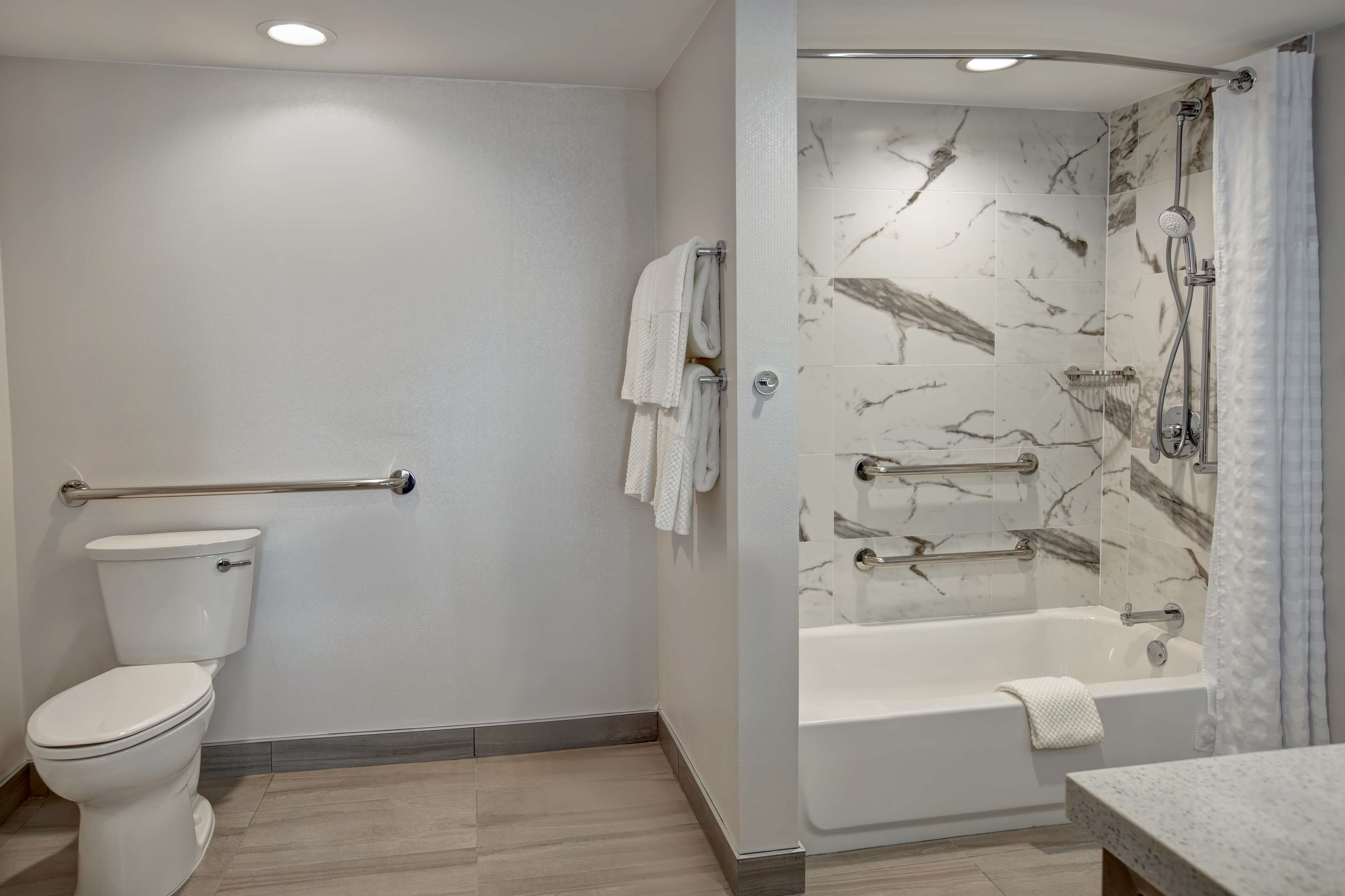 A modern bathroom with a toilet, a shower with marble walls, and a bathtub.