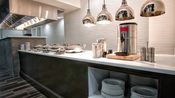 A modern kitchen with stainless steel appliances, a coffee station, and neatly stacked plates.