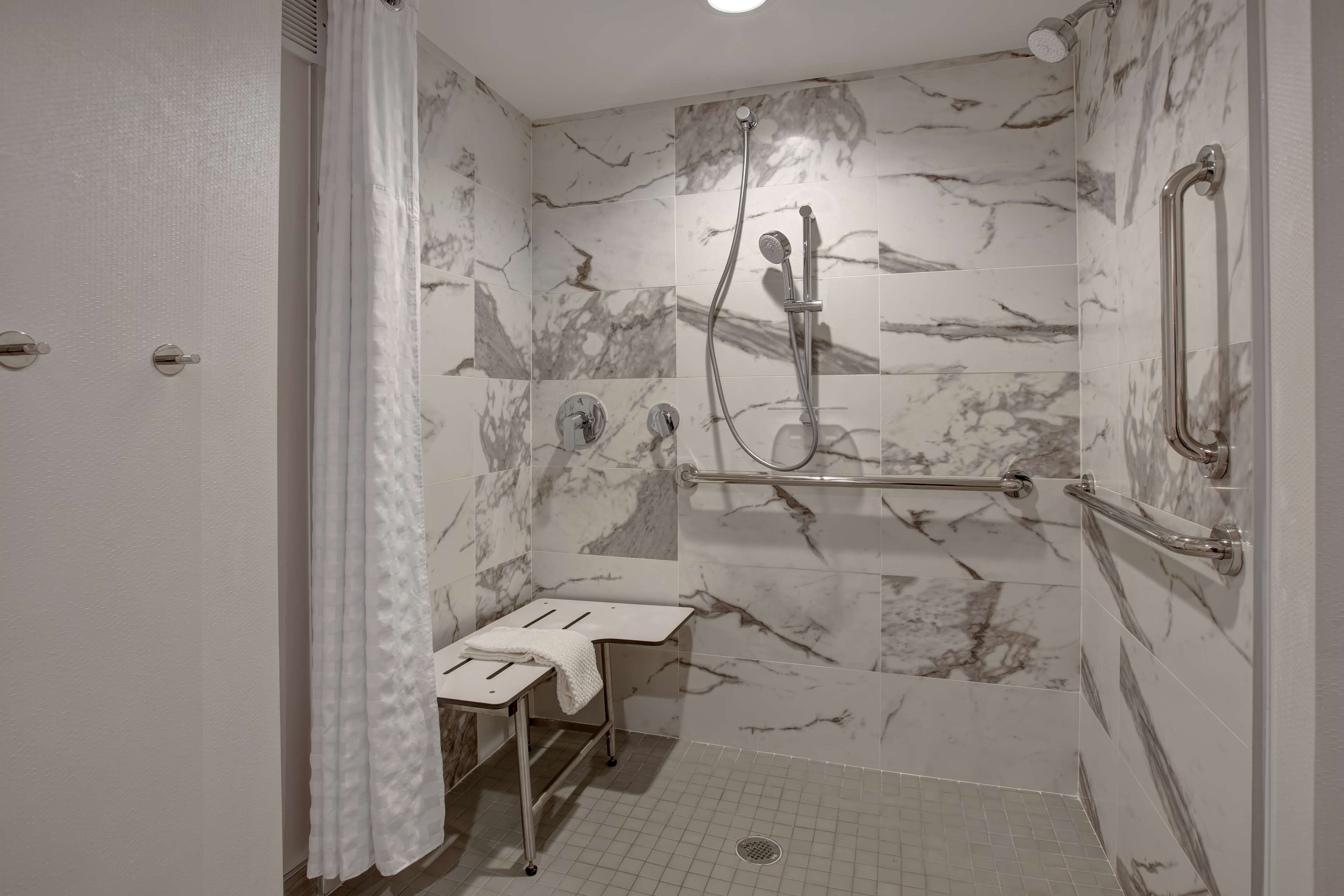A bathroom with a shower, marble walls, a towel rack, and a bench.
