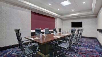 A conference room with a long table, multiple chairs, water bottles, and a flat-screen TV on the wall.