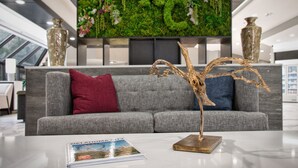 A modern lobby with a grey sofa, a decorative wooden sculpture, and a magazine on the table. - Embassy Suites by Hilton Oklahoma City Northwest (Oklahoma City)