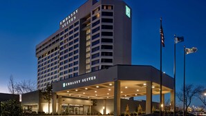 A modern hotel with a prominent "Embassy Suites" sign, a covered entrance, and a flagpole with flags. - Embassy Suites by Hilton Oklahoma City Northwest (Oklahoma City)