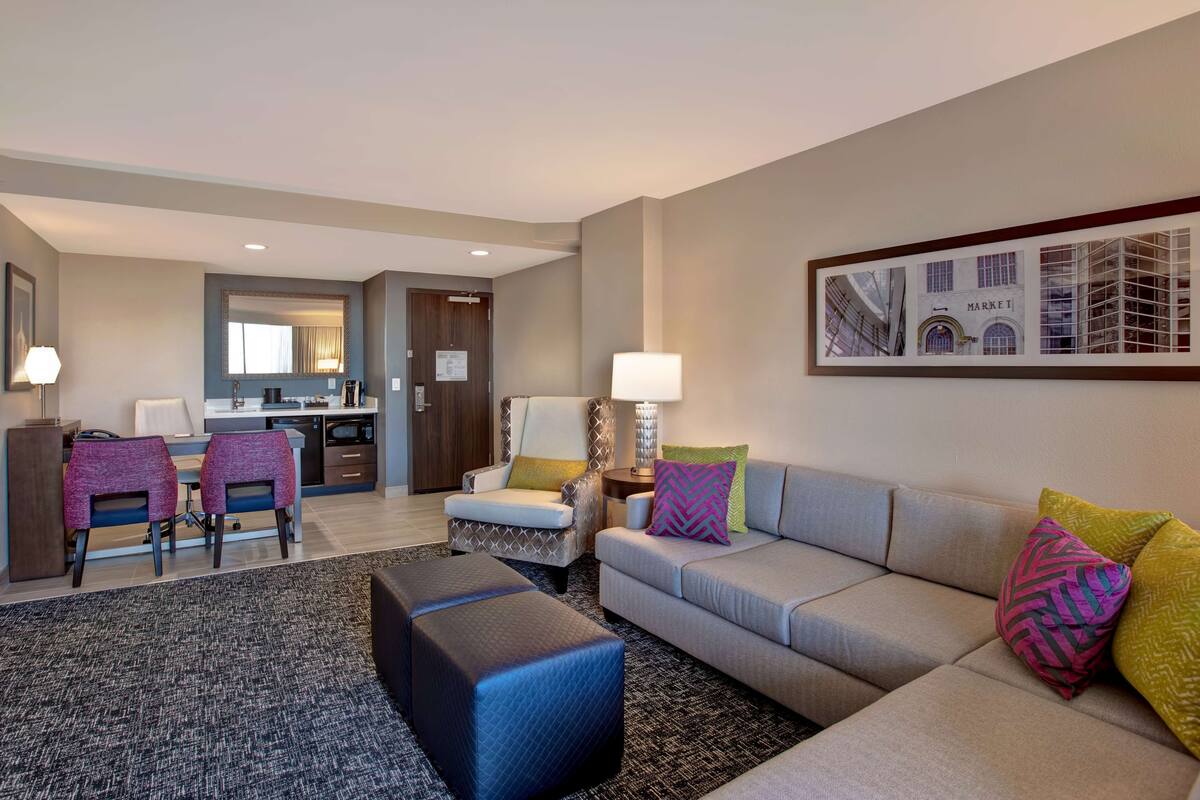 A modern hotel room with a living area, dining space, and a kitchenette.