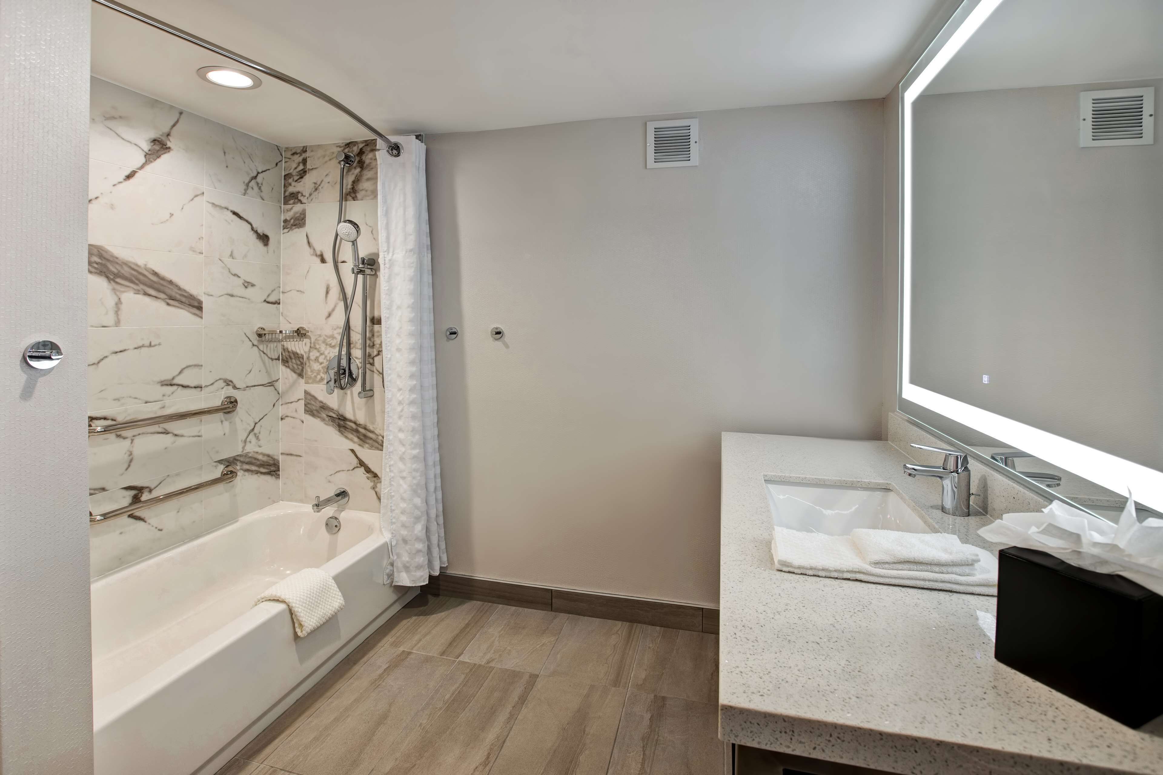A modern bathroom with a marble-tiled shower, a bathtub, a sink with a mirror, and a towel rack.