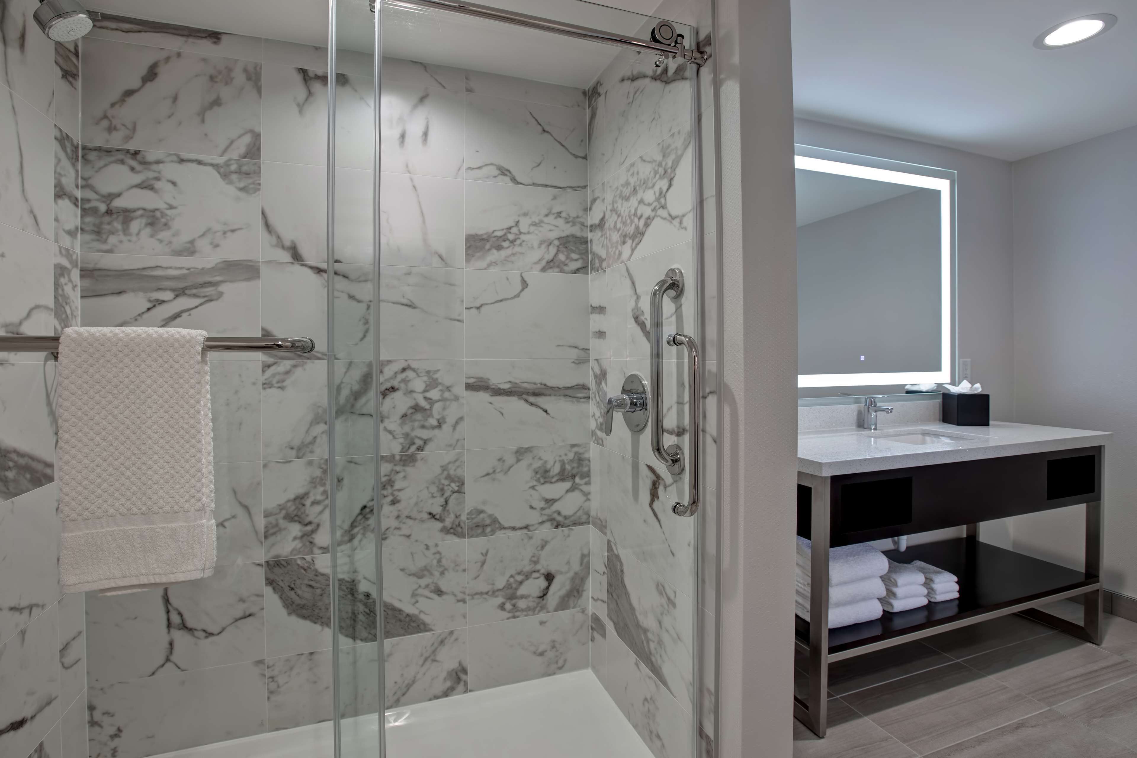 A modern bathroom with a glass-enclosed shower, marble tiles, a vanity with a mirror, and a towel rack.