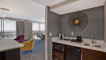 Una habitación de hotel moderna con kitchenette, un gran elemento decorativo en la pared y vistas de la ciudad a través de amplios ventanales.