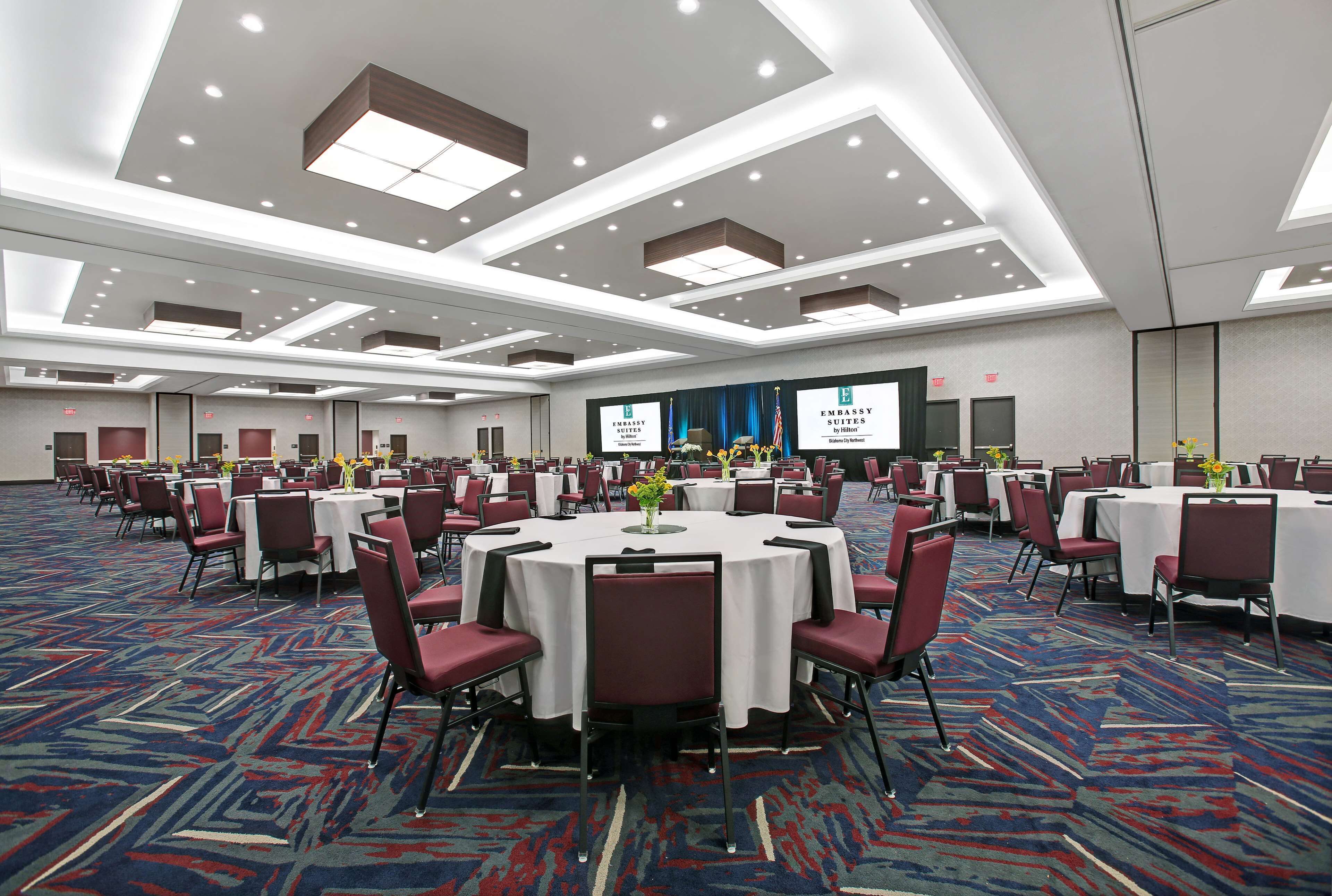 A large conference room with multiple round tables, red chairs, and a carpeted floor.