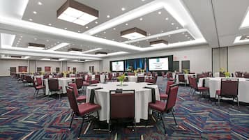 A large conference room with multiple round tables, red chairs, and a carpeted floor.