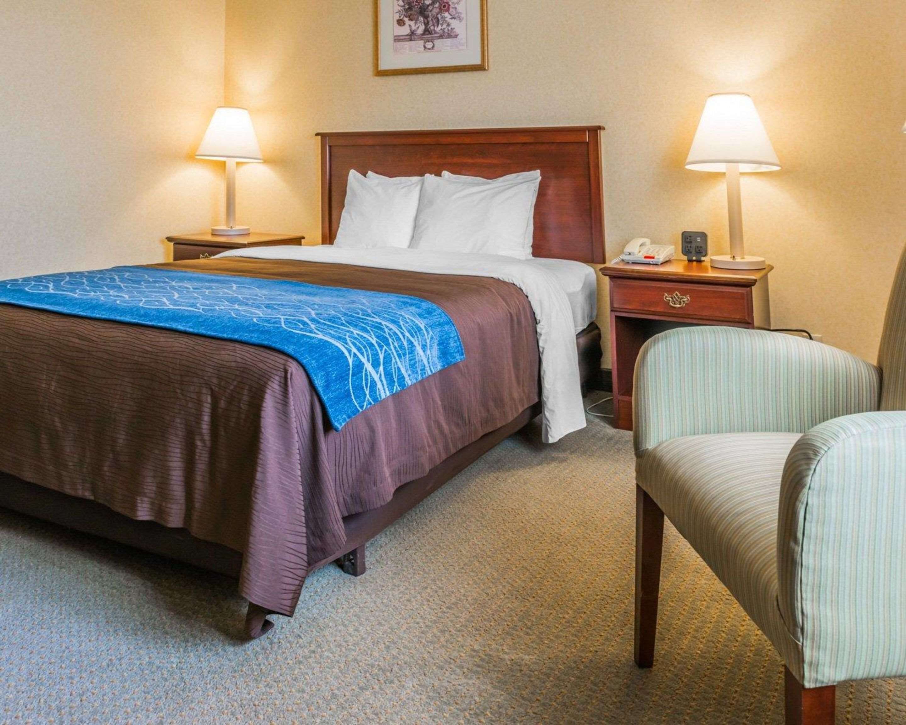 A hotel room with a large bed, two bedside tables, a chair, and a nightstand with a lamp.