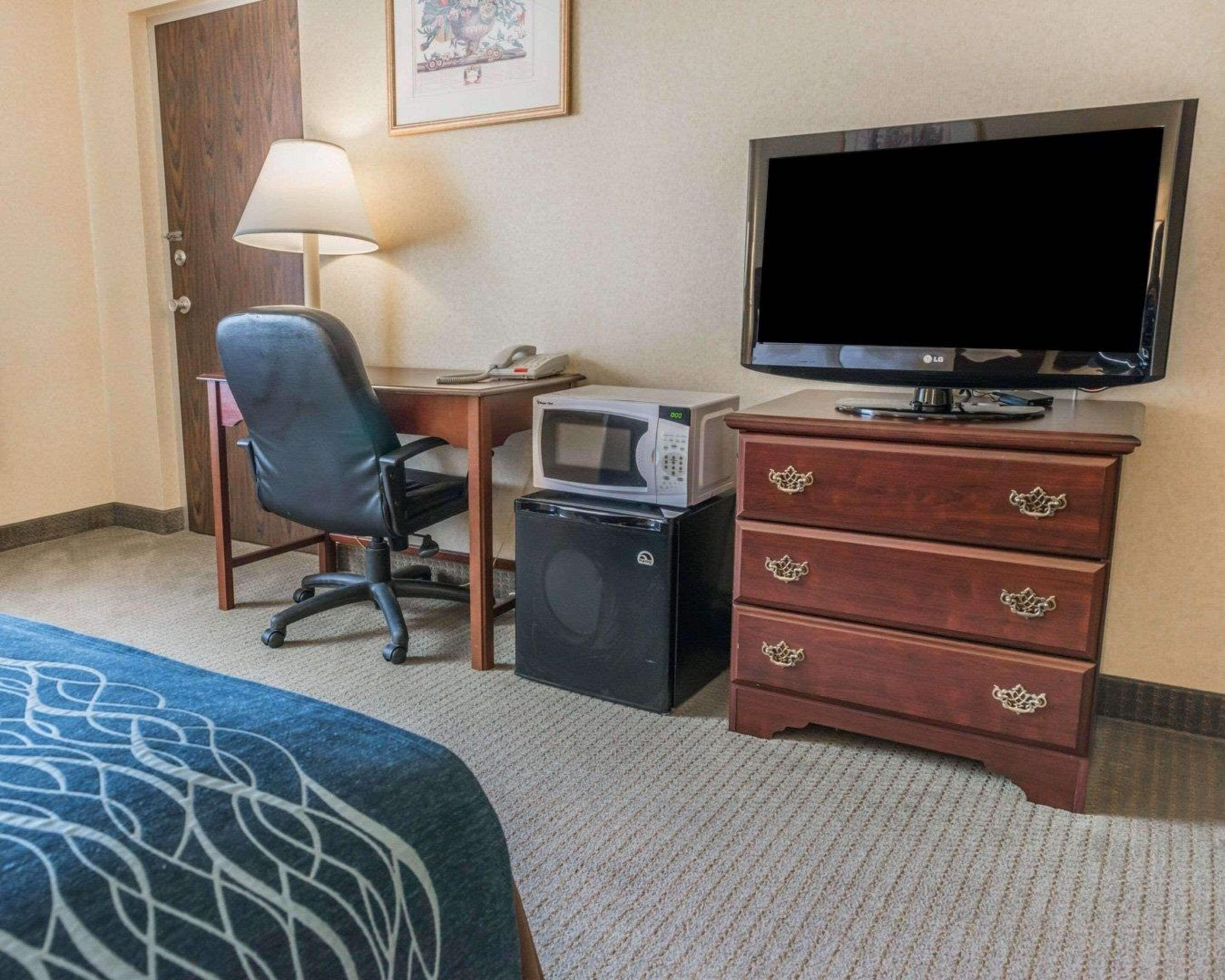 A hotel room with a bed, a desk with a lamp, a television, a microwave, and a dresser.