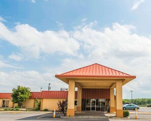 A building with a red roof and beige walls, featuring a covered entrance and a parking lot.