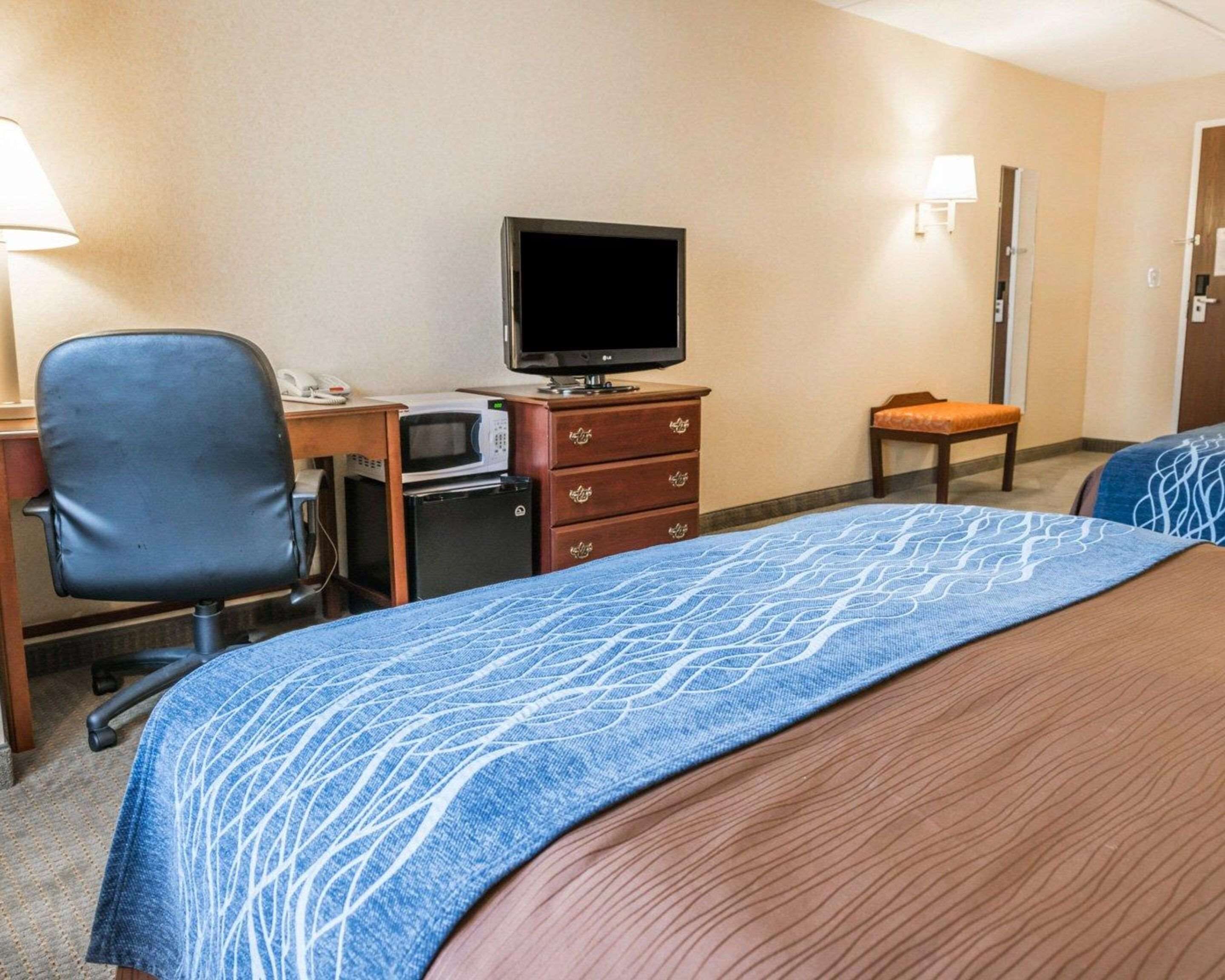 A hotel room with a bed, a desk with a computer, a microwave, a television, and a chair.