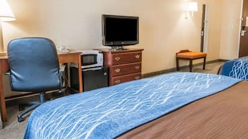 A hotel room with a bed, a desk with a computer, a microwave, a television, and a chair.