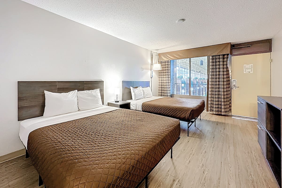 Hotelkamer met twee bedden, een kledingkast, een bureau en een raam met gordijnen.