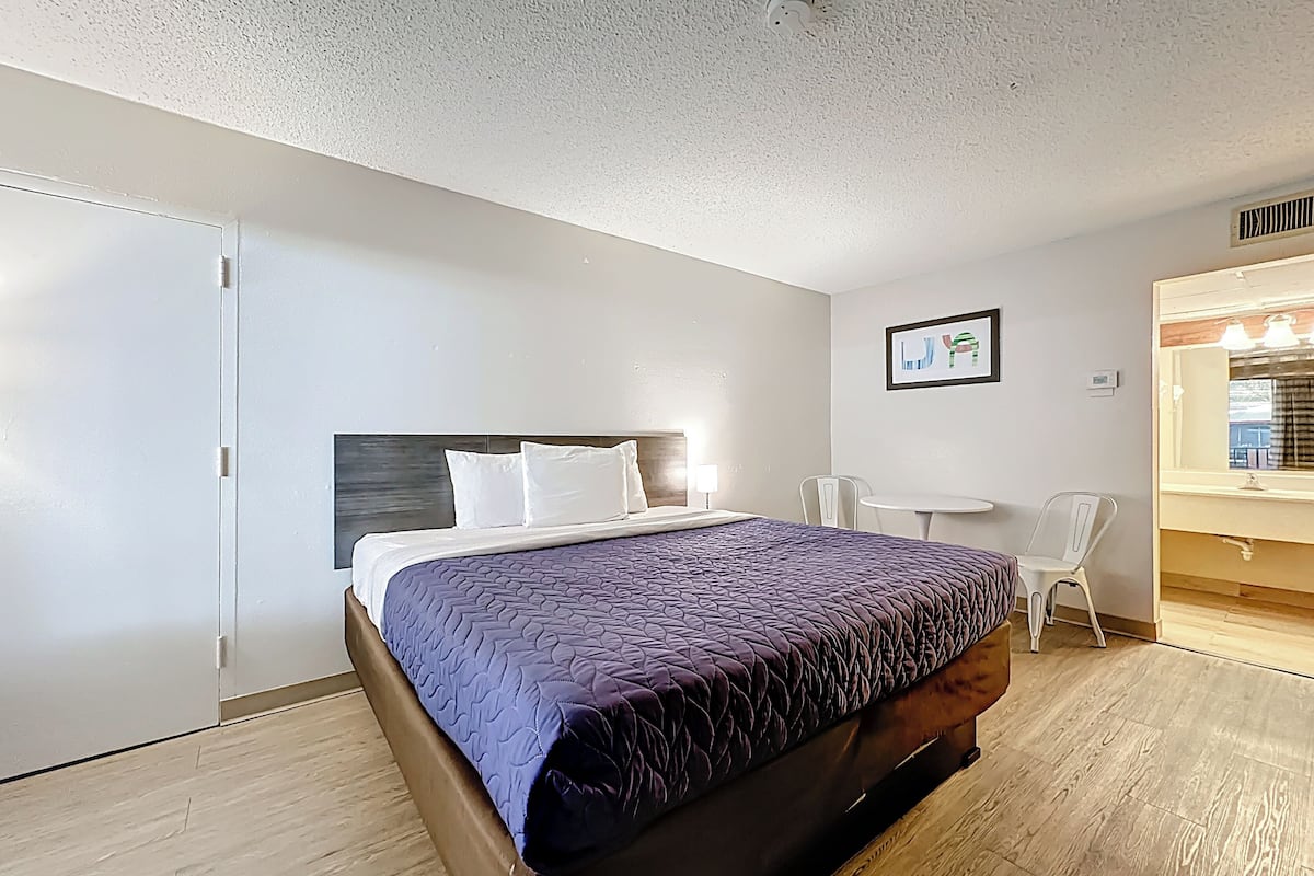Een hotelkamer met een bed, een bureau, een stoel, een klein tafeltje en een spiegel.