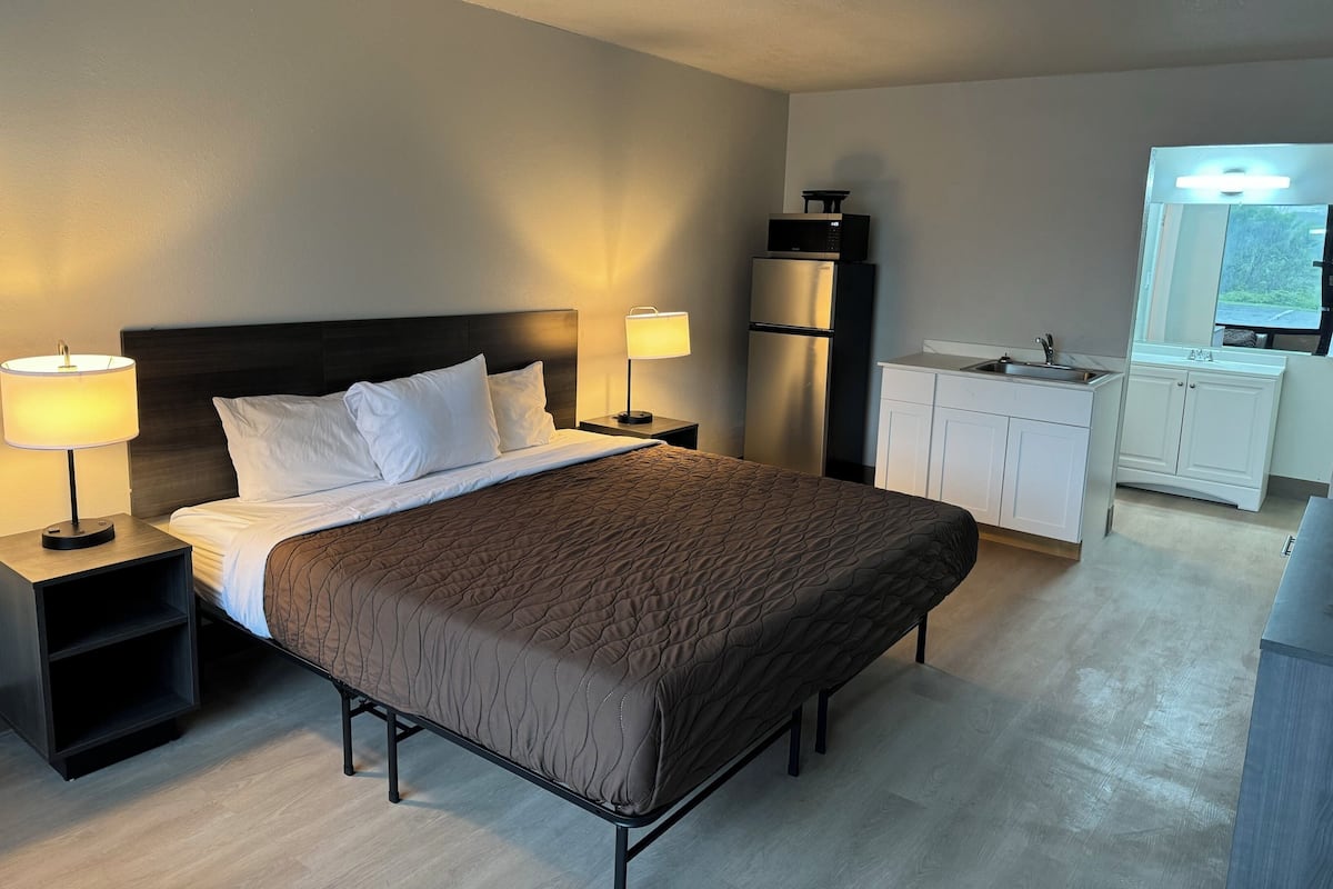 Hotelkamer met een bed, nachtlampjes, een koelkast, een klein tafeltje, een wastafel en een spiegel.