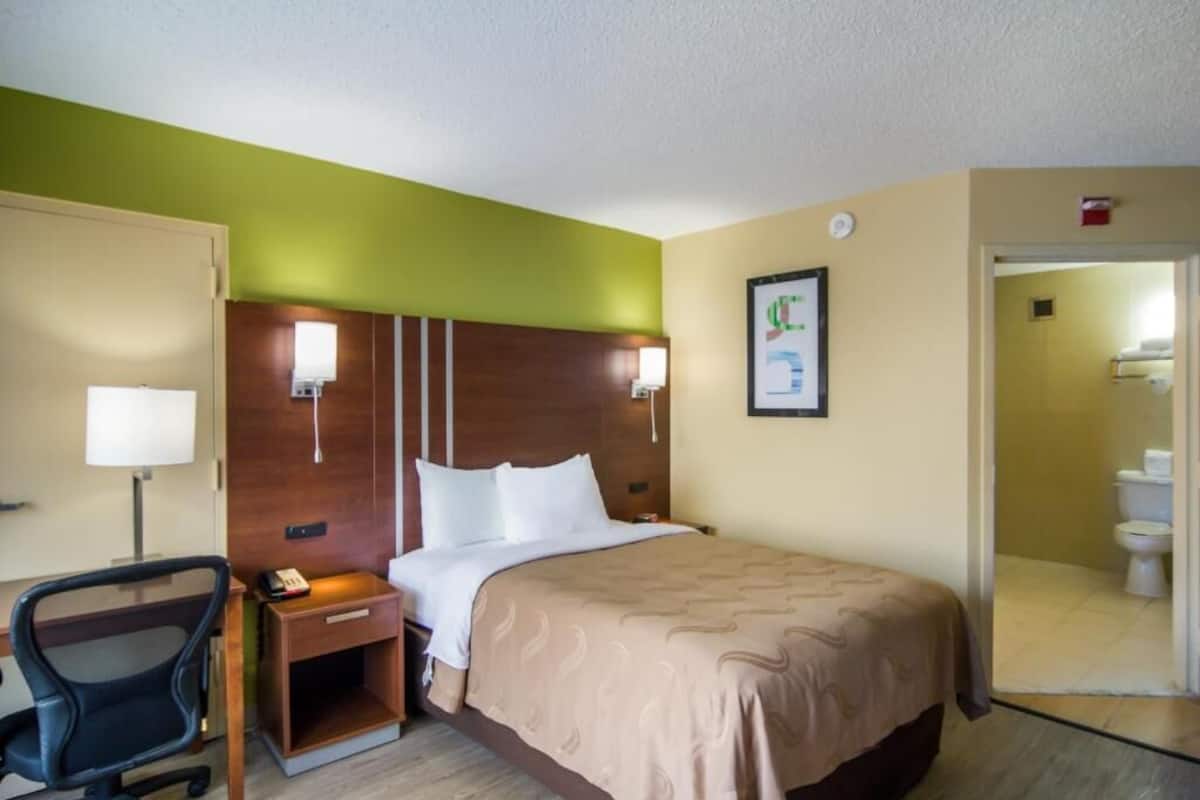 Een hotelkamer met een bed, een bureau, een stoel en een badkamer, zichtbaar door een geopende deur.