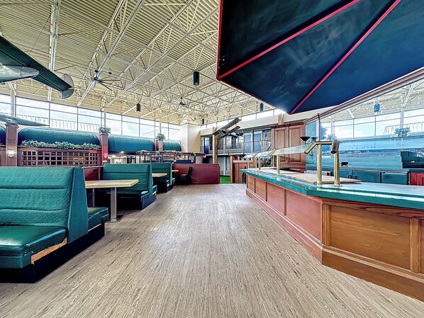 A restaurant with green booths, wooden tables, and a bar area with a view of the water.