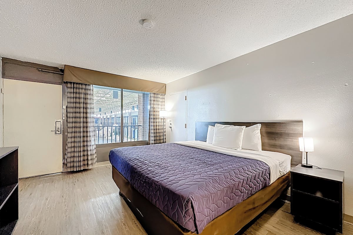 Hotelkamer met een groot bed, een nachtkastje, een lamp en uitzicht door een raam.