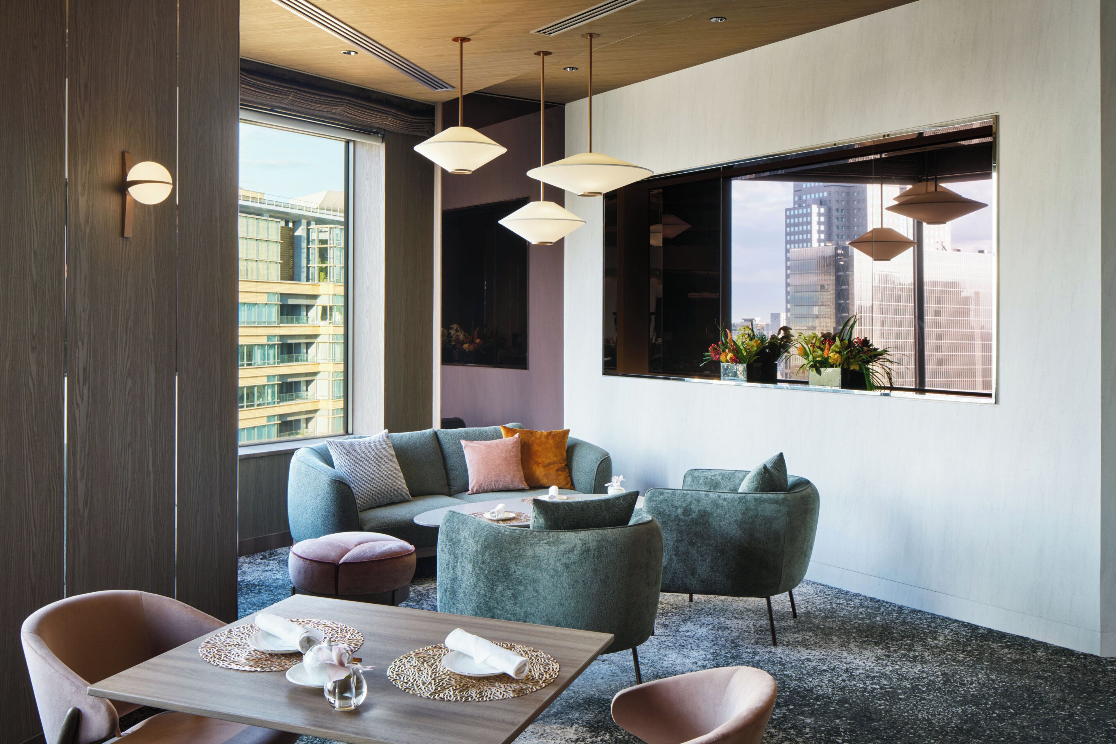 A modern hotel room with a large window, a sofa set, a dining table, and pendant lighting.