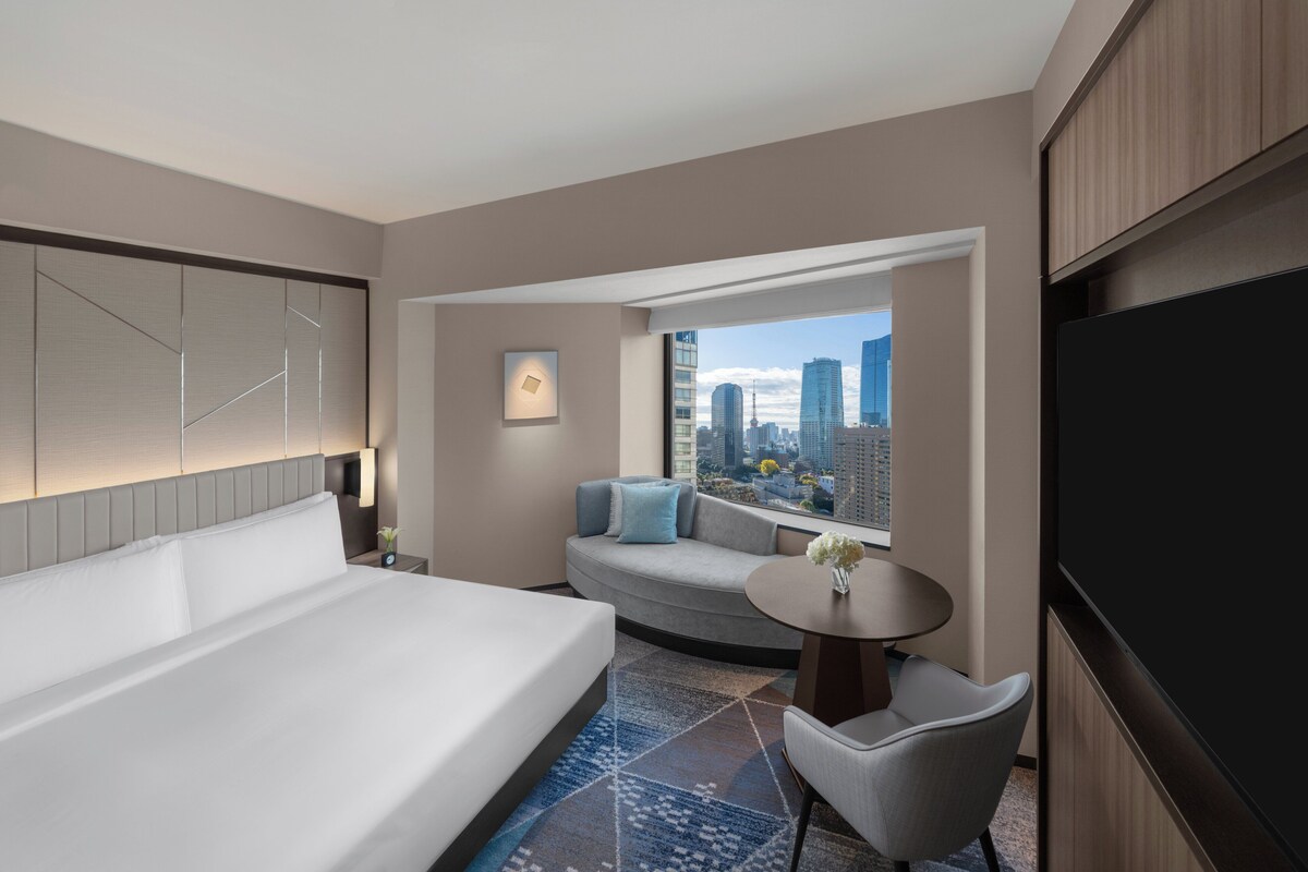 A modern hotel room with a large bed, a sofa, a small table, and a TV.
