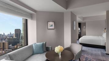Ein modernes Hotelzimmer mit Blick auf die Stadt, einer Couch, einem runden Tisch mit einer Vase und einem Bett.