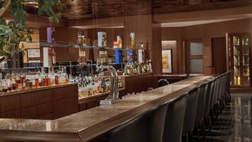 A bar area with a long counter, multiple seating options, and a variety of bottles and glasses.