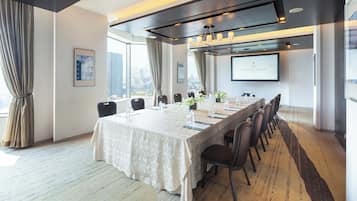 Un salón de conferencias con una larga mesa, sillas, una pantalla de proyector y vistas a la ciudad.