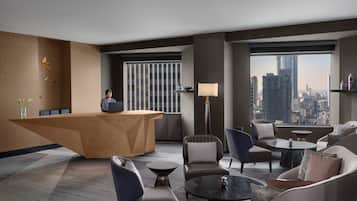 A modern hotel lobby with a reception desk, seating area, and large windows offering a city view.