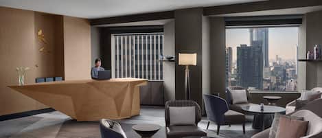 A modern hotel lobby with a reception desk, seating area, and large windows offering a city view.