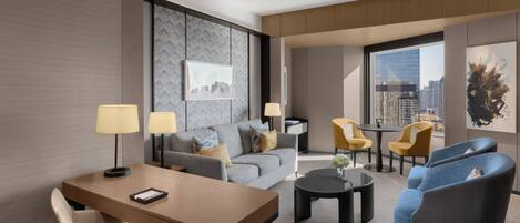 A modern hotel room with a sofa, armchairs, a dining table, and a city view.