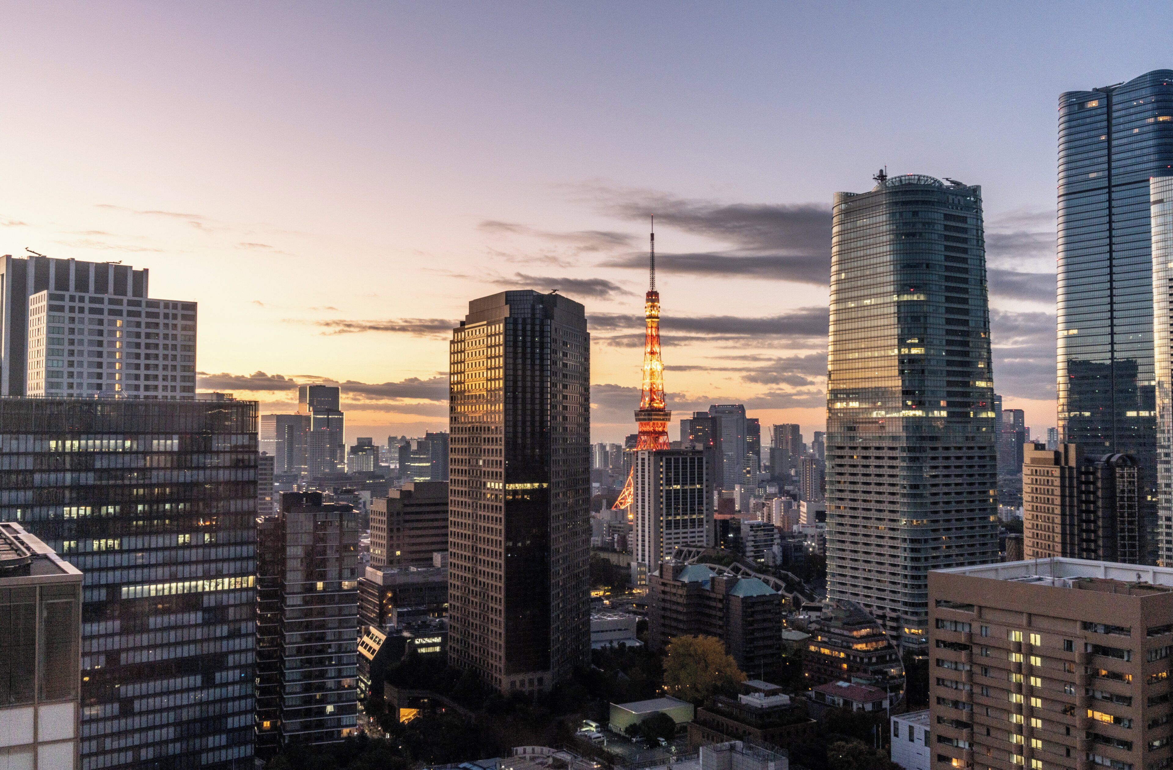 A cityscape with modern skyscrapers and the Eiffel Tower illuminated against a sunset sky.
