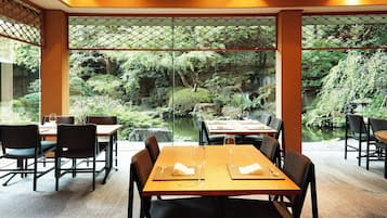 A restaurant with tables and chairs, a view of a garden through glass partitions, and a wooden ceiling.