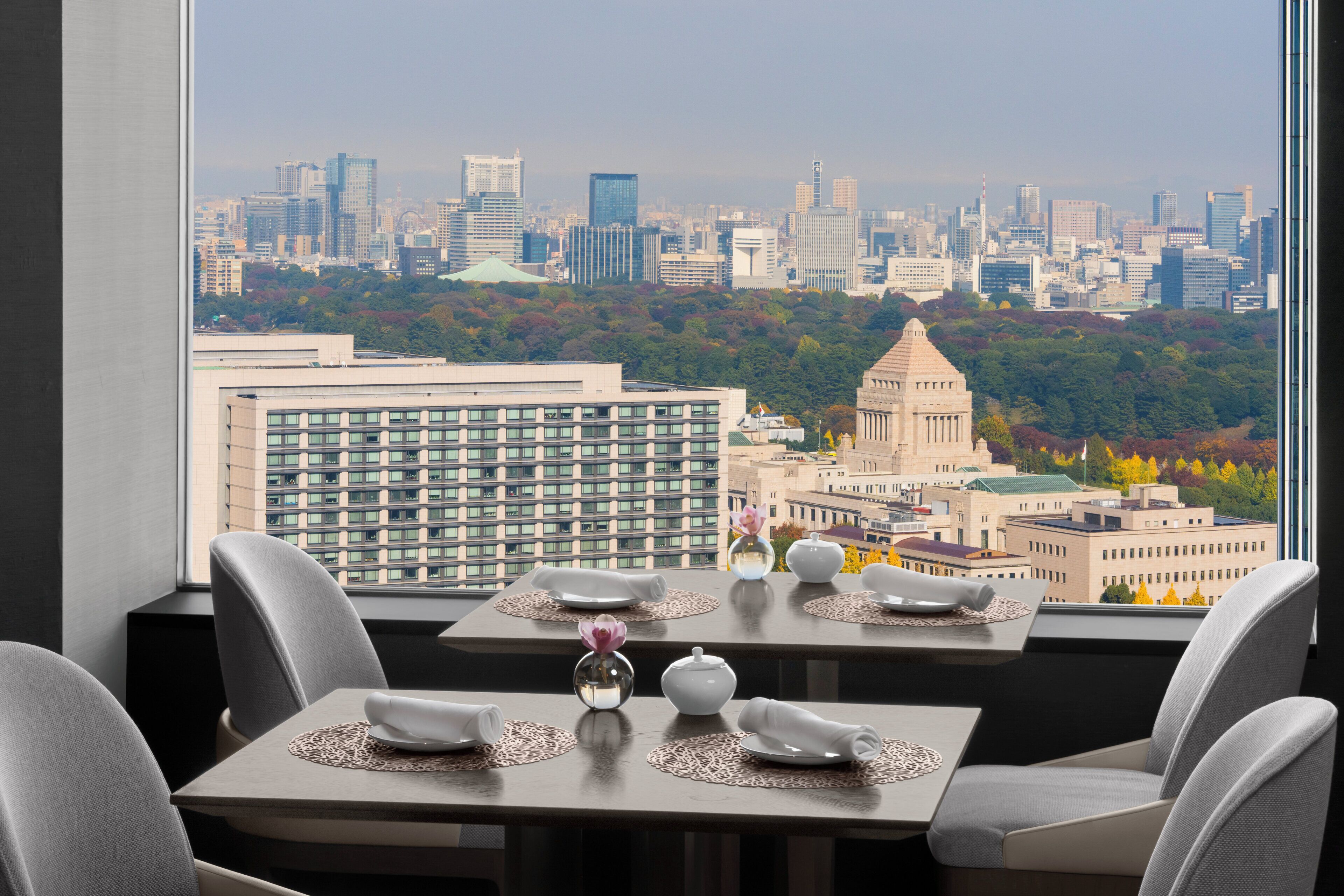 A dining area with tables set for two, overlooking a cityscape with modern buildings and a historic building.