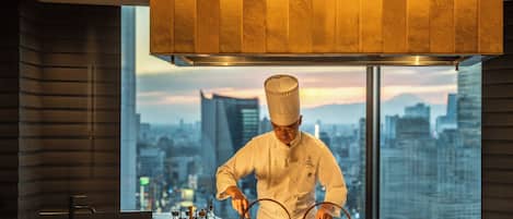 Un chef preparando comida en una cocina moderna con vista a la ciudad.