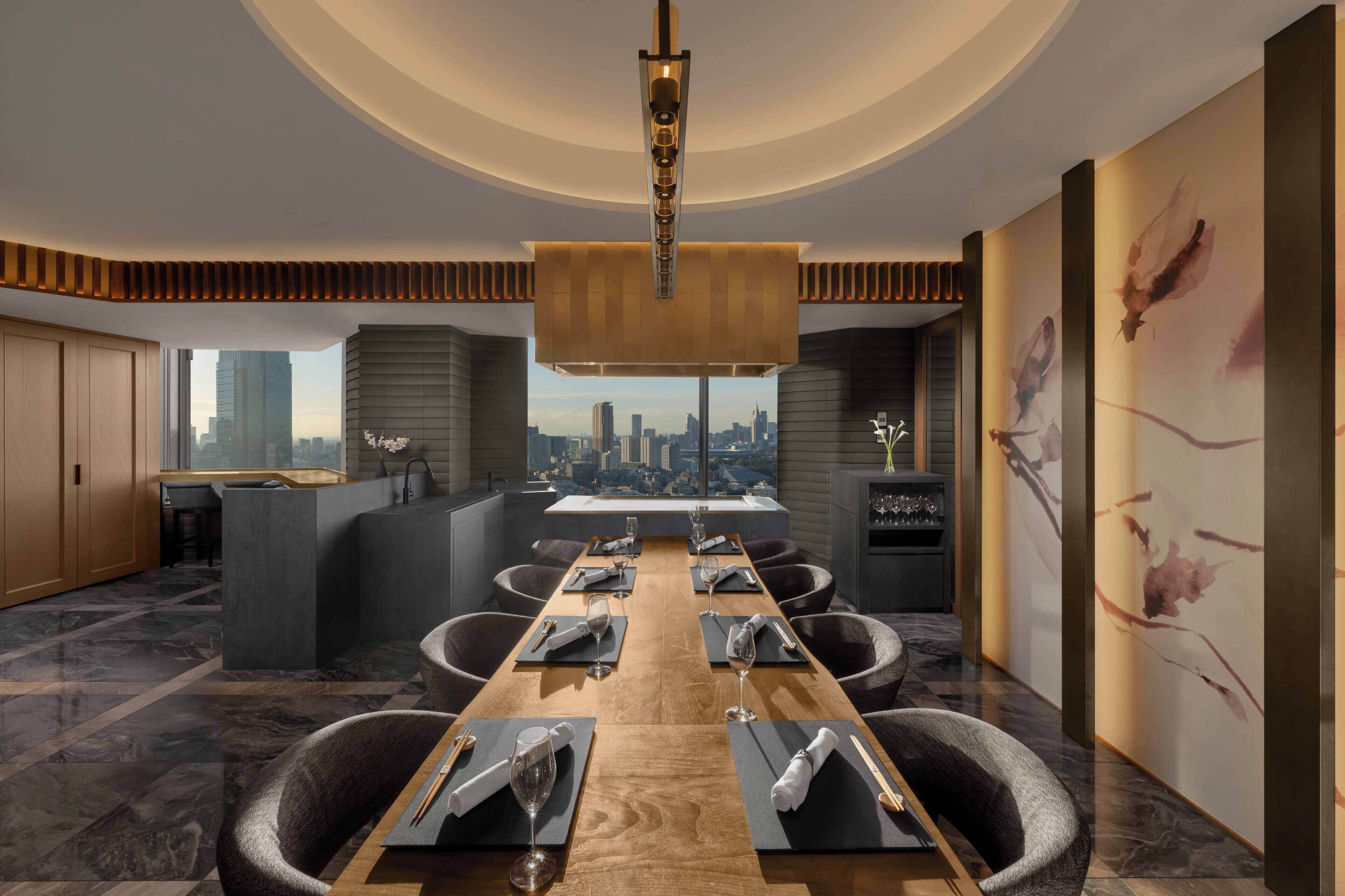 Un comedor moderno con una mesa larga dispuesta para seis personas, vista a la ciudad a través de amplias ventanas y una lámpara de araña contemporánea.